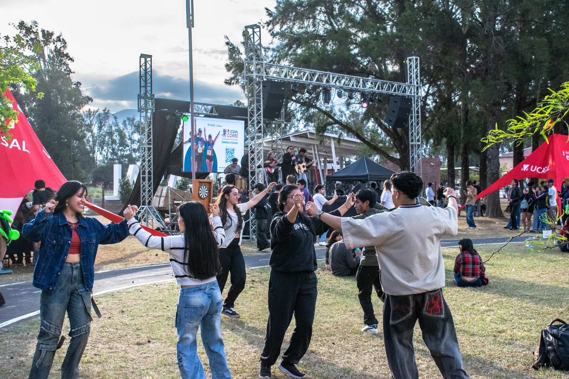 Estudiantes bailan en ronda frente al escenario al aire libre.